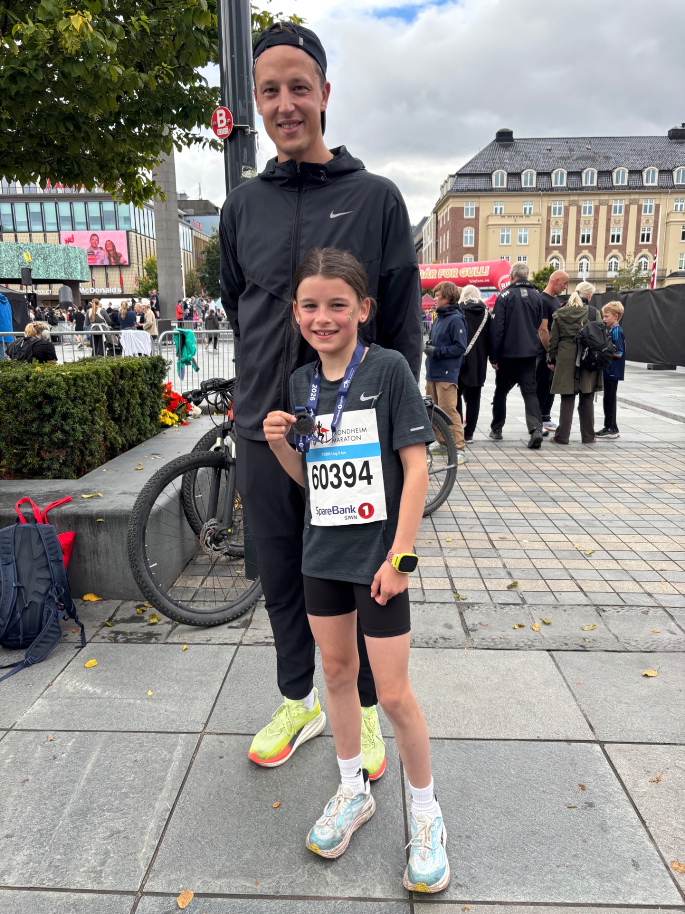 Jente med medalje og startnummer fra Trondheim Maraton sammen med en voksen leder